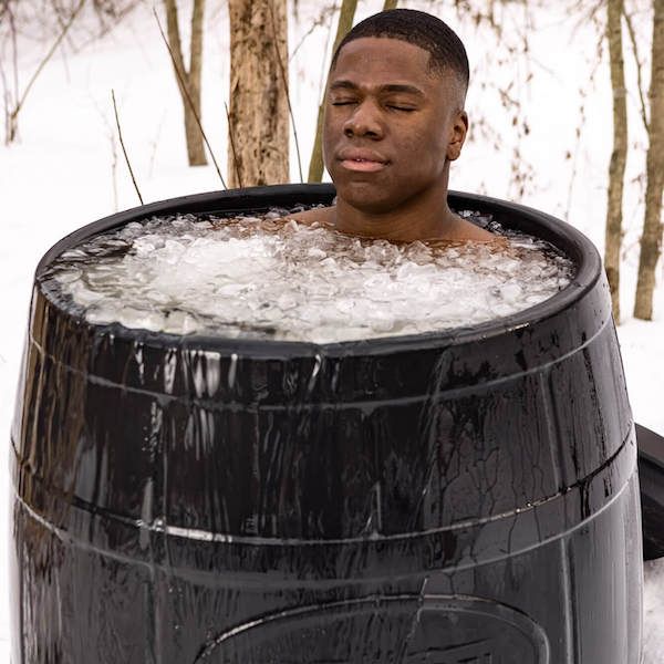 Person immersed in an ice barrel in a snowy outdoor setting