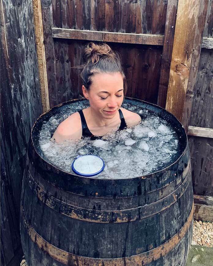 Woman immersed in an outdoor barrel ice bath filled with ice