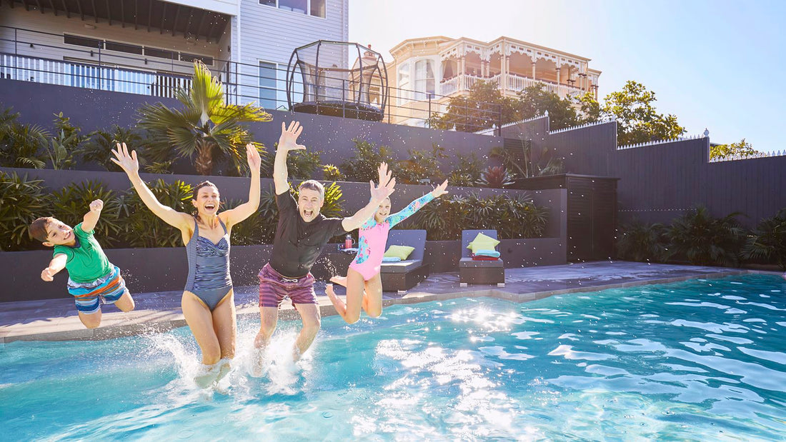 Family of four laughing and jumping into a modern residential backyard swimming pool